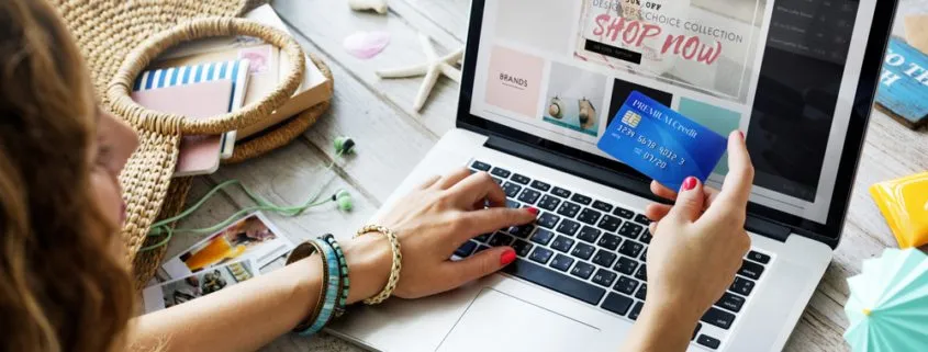 Pessoa segurando um cartão de crédito enquanto faz uma compra numa loja virtual pelo notebook